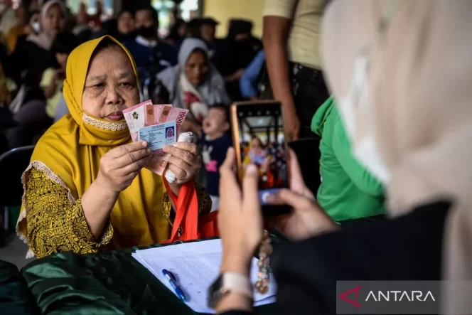 
 Arsip - Petugas memotret warga memperlihatkan uang tunai saat penyaluran bantuan sosial di Kota Tangerang, Banten, Selasa (12/8/2025). Pemerintah Provinsi Banten telah menyalurkan bantuan sosial senilai Rp9,25 miliar kepada 18.500 keluarga penerima manfaat (KPM) dari total anggaran Rp18,8 miliar untuk 37.741 KPM pada tahun 2025. ANTARA FOTO/Putra M. Akbar/foc.